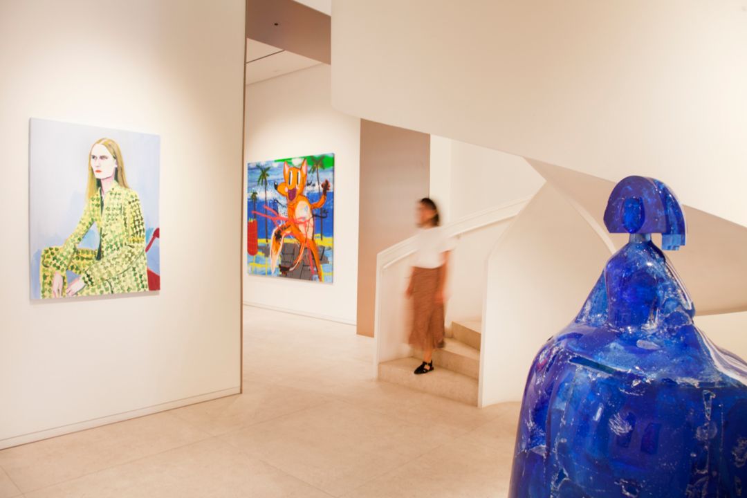 Art gallery with a blue sculpture in the foreground and two colorful paintings on the walls.