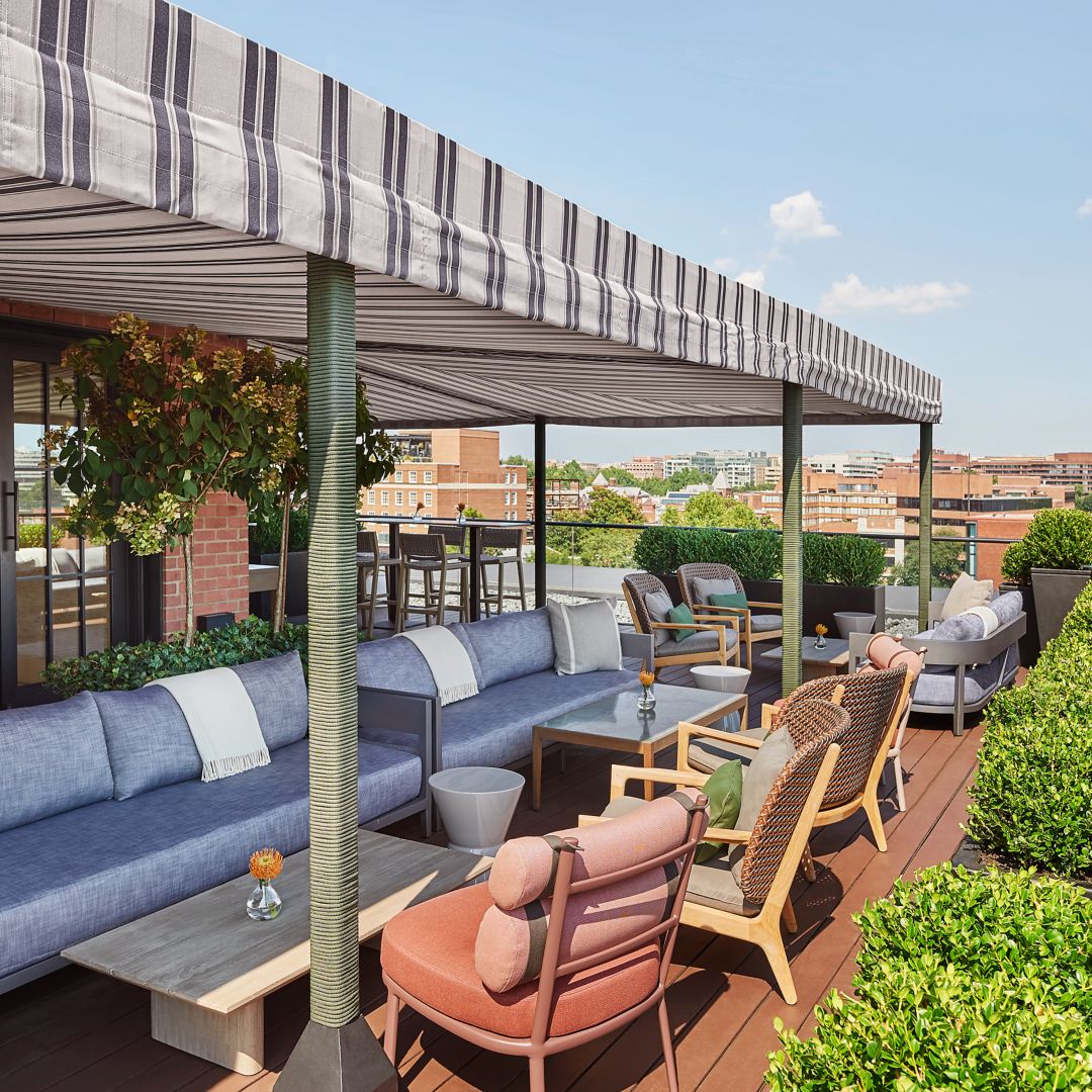 A rooftop bar in Georgetown with striped canopy, seating area, potted plants, and a view of DC.