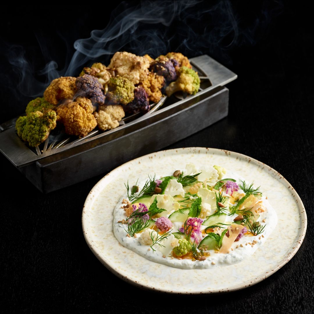 A dish with cauliflower, herbs, and sauce, with roasted cauliflower in the background.