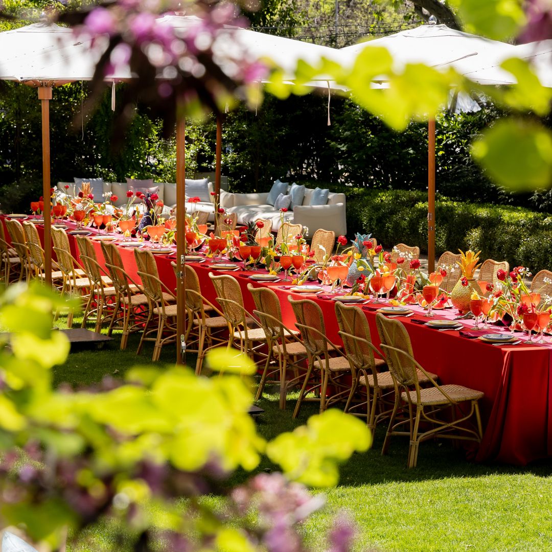 terraza ajardinada al sol con mesa imperial para eventos, con sombrillas blancas y flores