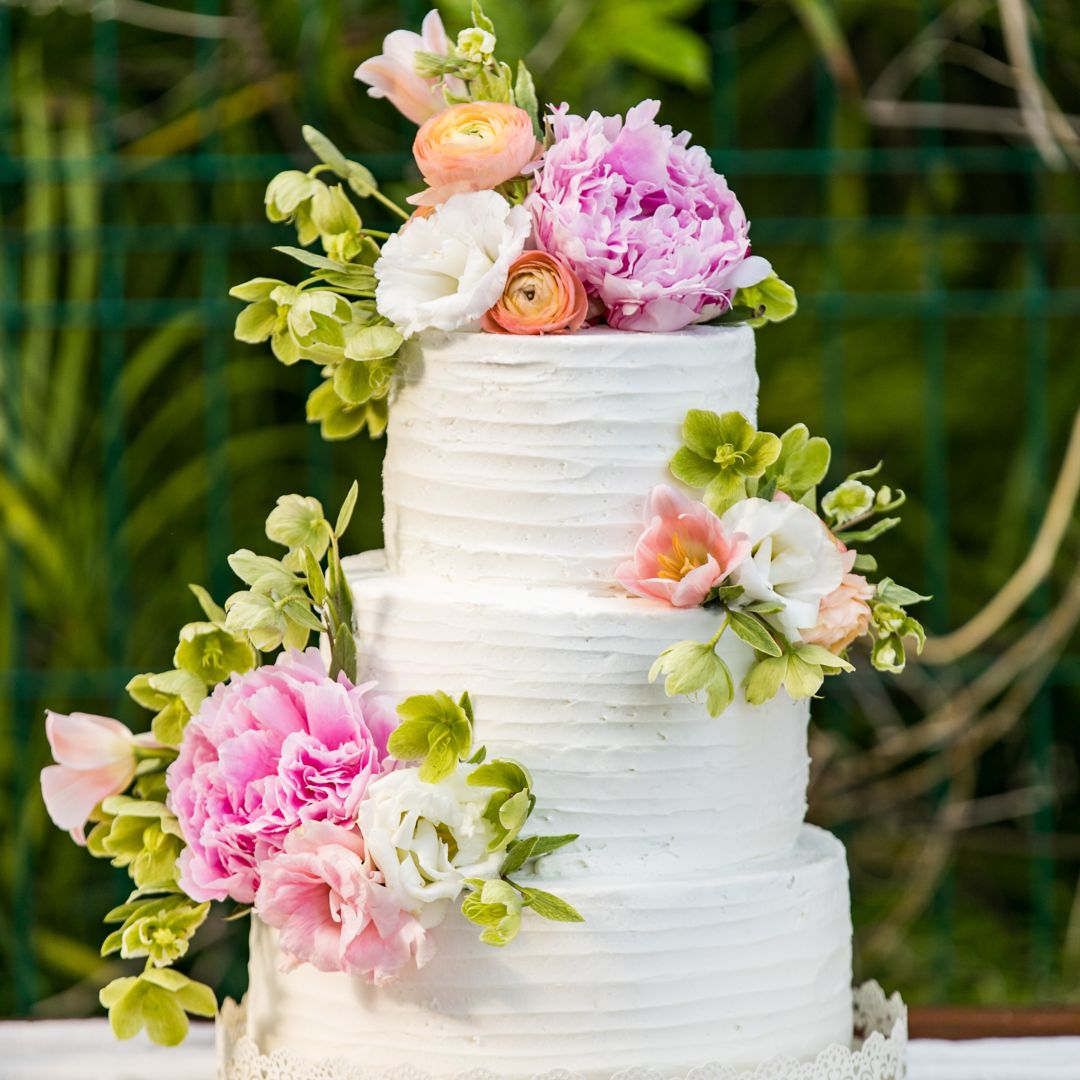 Three tier wedding cake with white frosting decorated with pink flowers